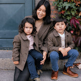 Mor og børn iført brune uldfrakker foran grøn dør