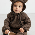 Baby i brun heldragt med ører, sidder og kigger op