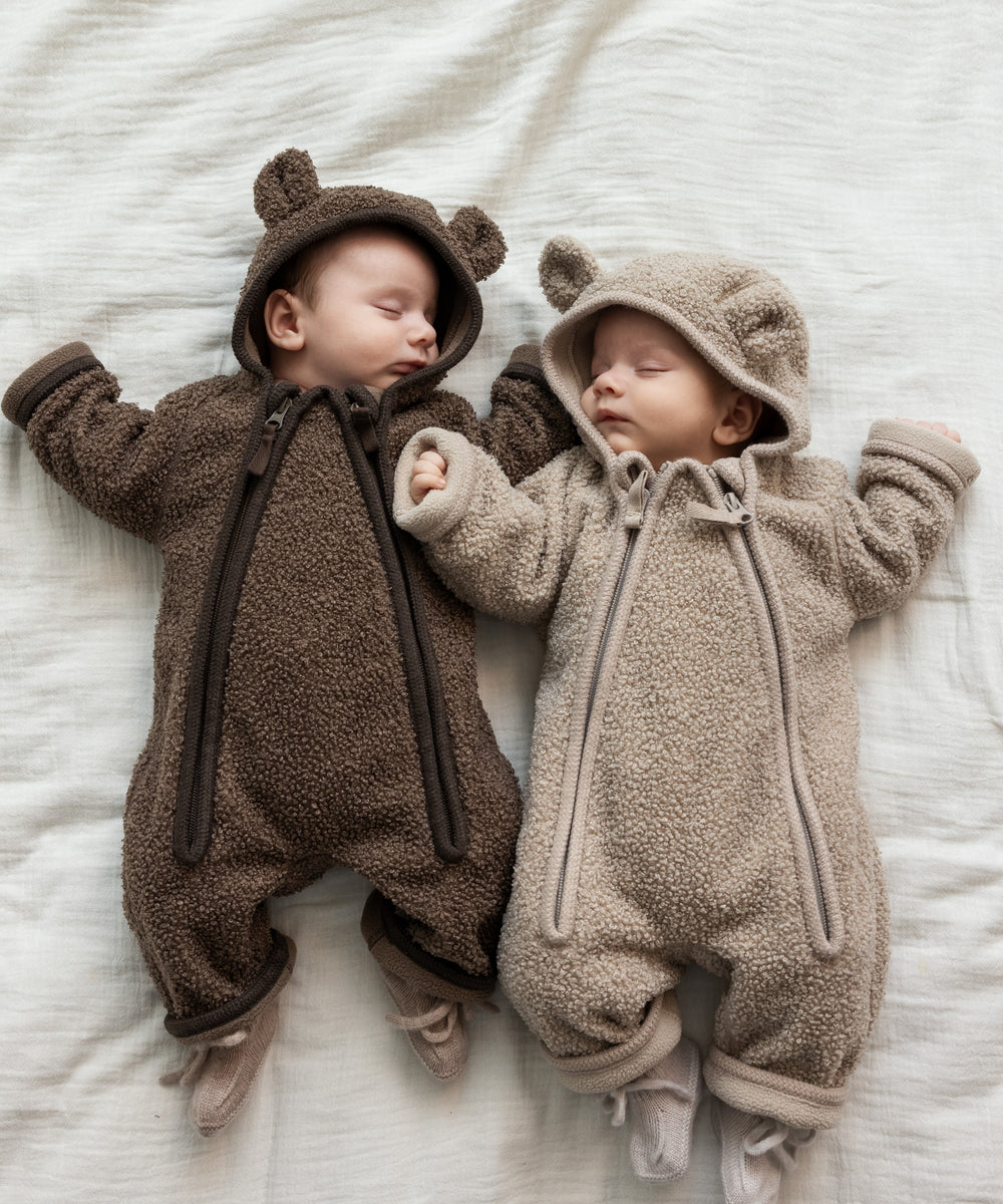 To babyer liggende iført teddyheldragter i lyse og mørke brune nuancer