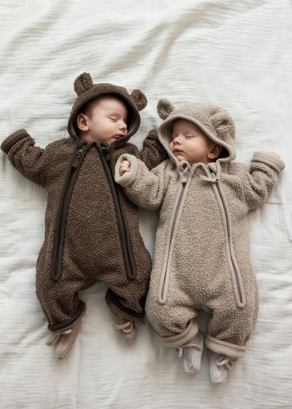 To babyer liggende iført teddyheldragter i lyse og mørke brune nuancer