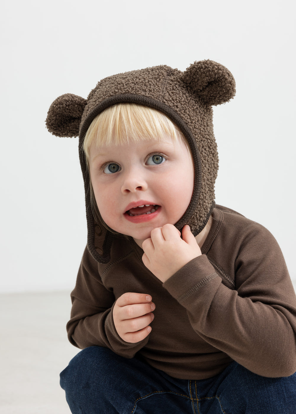 Barn iført brun elefanthue med ører i teddyfleece, sidder og kigger op