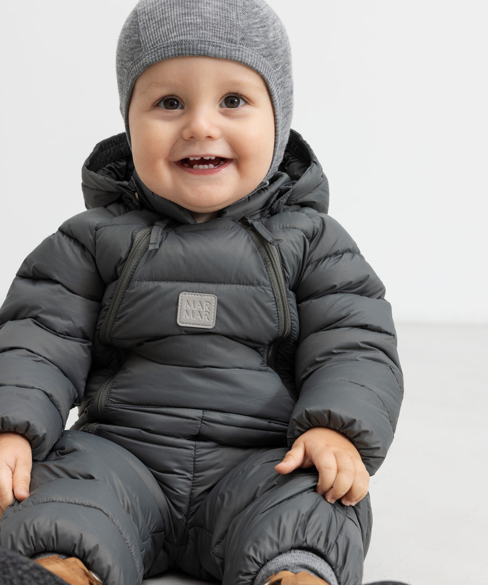 Smilende baby i mørkegrå dundragt sidder på gulv