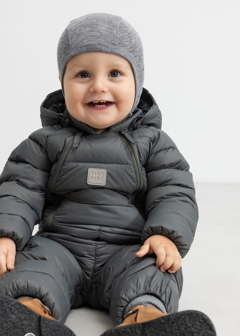 Smilende baby i mørkegrå dundragt sidder på gulv