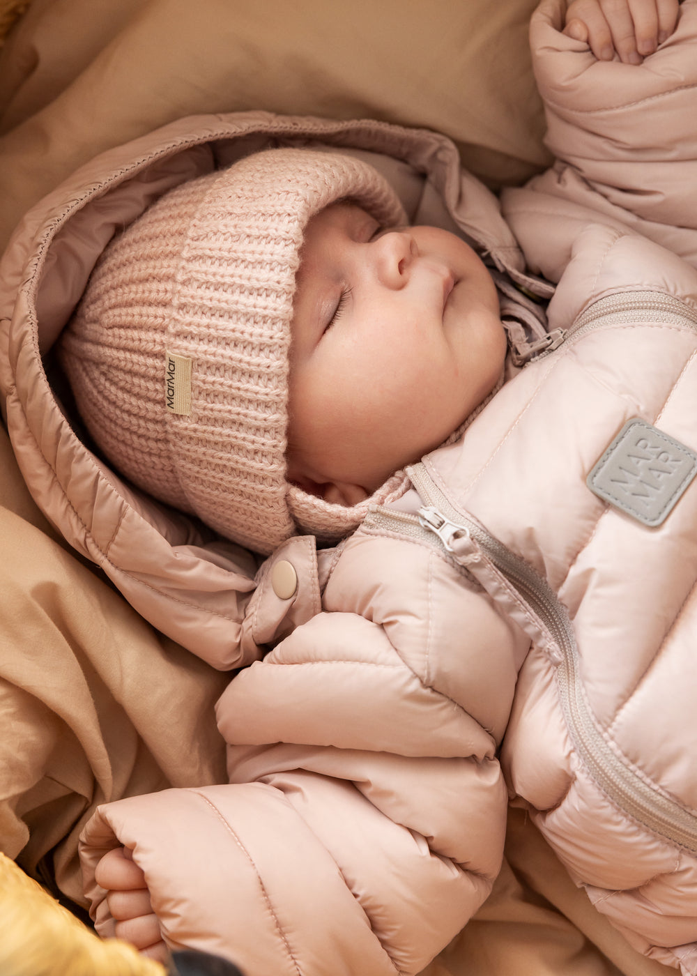 Baby iført lyserød dundragt og strikket hue