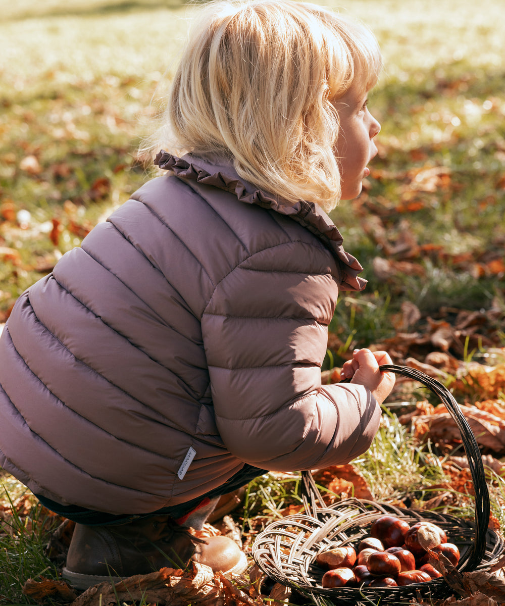 Børn bøjer sig ned iført rosa vatteret jakke med flæsekrave i naturen