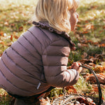 Børn bøjer sig ned iført rosa vatteret jakke med flæsekrave i naturen