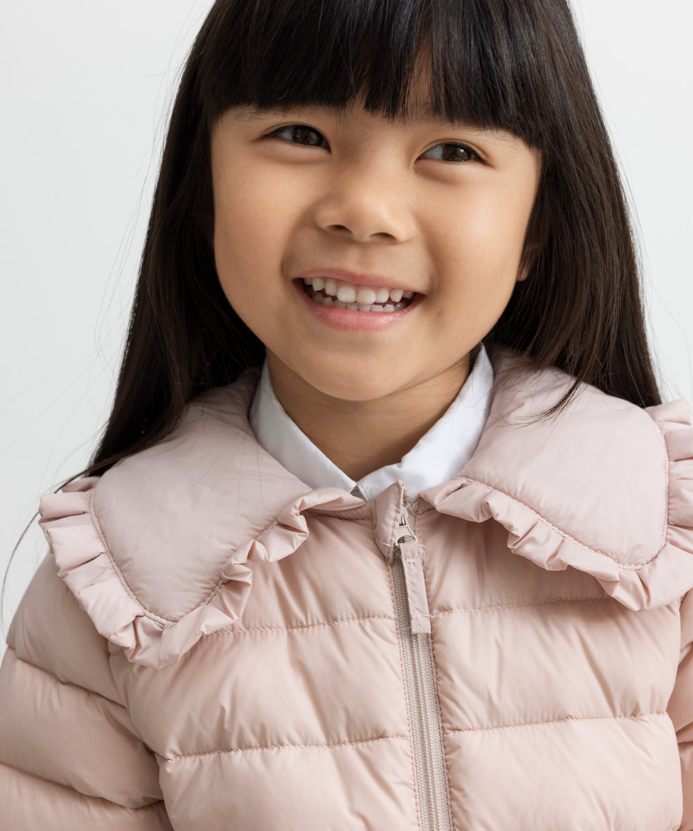 Barn i lyserød vatteret jakke med flæsekrave smiler