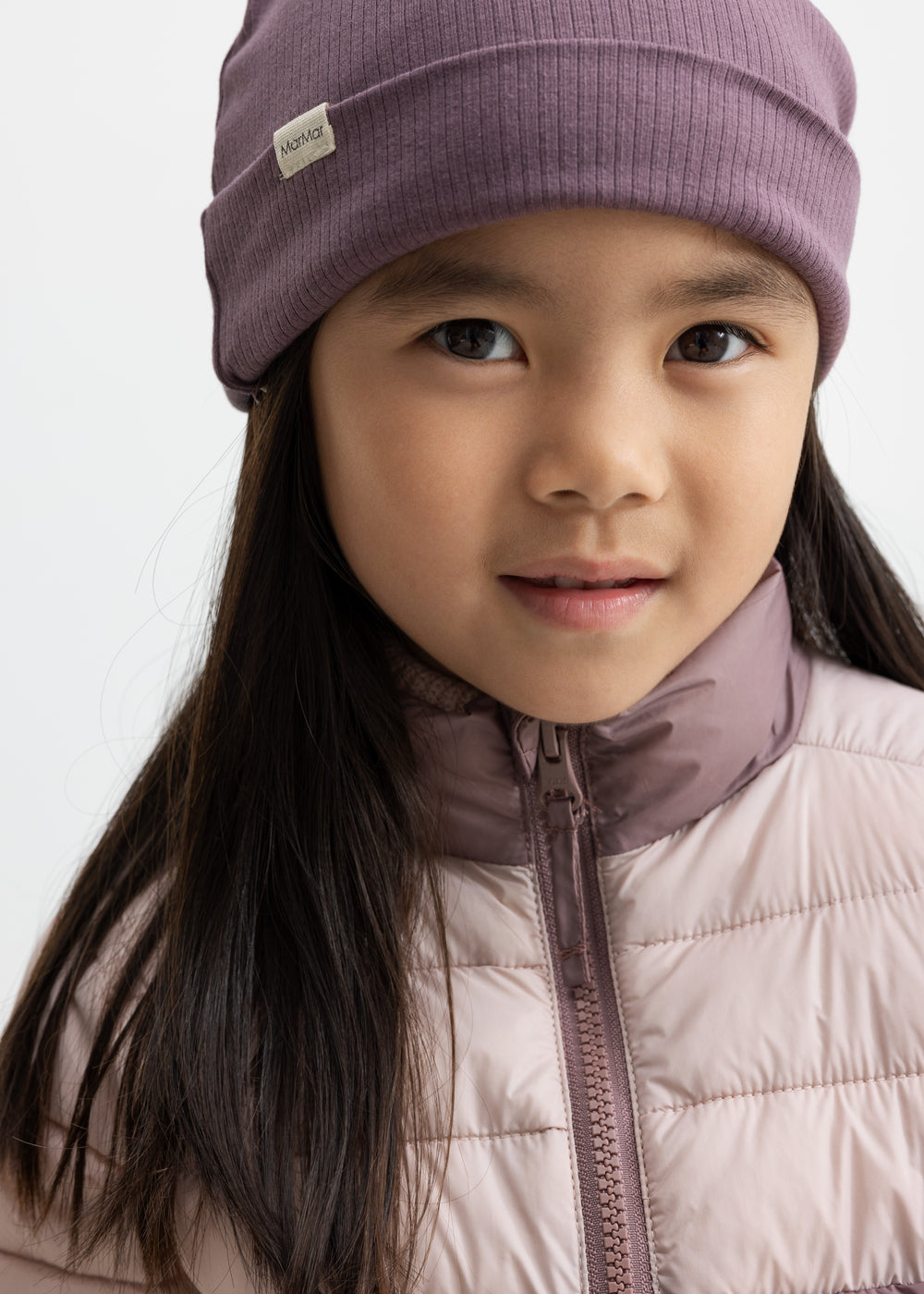 Pige iført vatteret jakke i rosa og lilla med matchende hue