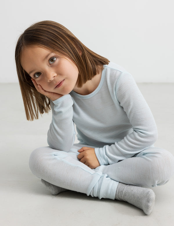 Pige i lyseblåt ribtøj, der sidder på gulvet med hovedet hvilende i hånden