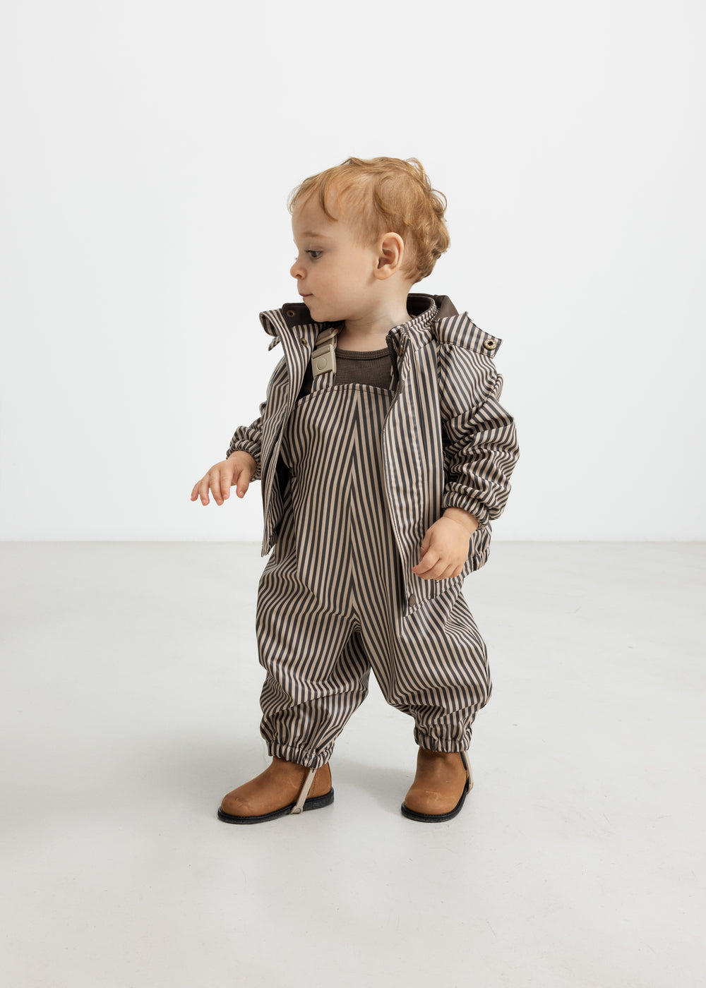 Baby i regnsæt med brune striber og hætte, står op