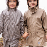 To børn iført regntøj på stranden, det ene barn i beige regnjakke og bukser