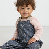 Barn iført mørkeblå regnbukser med print og lyserød trøje, sidder ned