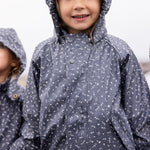 Barn iført mørkeblåt regnsæt med hætte, smilende og kigger op