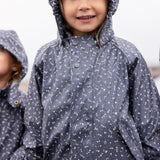 Barn iført mørkeblåt regnsæt med hætte, smilende og kigger op