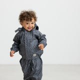 Baby i mørkeblåt regnsæt med småprint og hætte, smilende og iført lyserøde gummistøvler