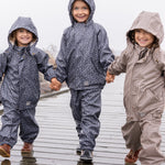 Tre børn i regntøj, midterste barn iført mørkeblåt sæt med print og hætte