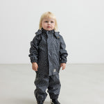 Barn i mørkeblå regnjakke med print og sorte støvler, står rakt op