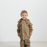 Barn iført beige regnsæt og gummistøvler, står og kigger op