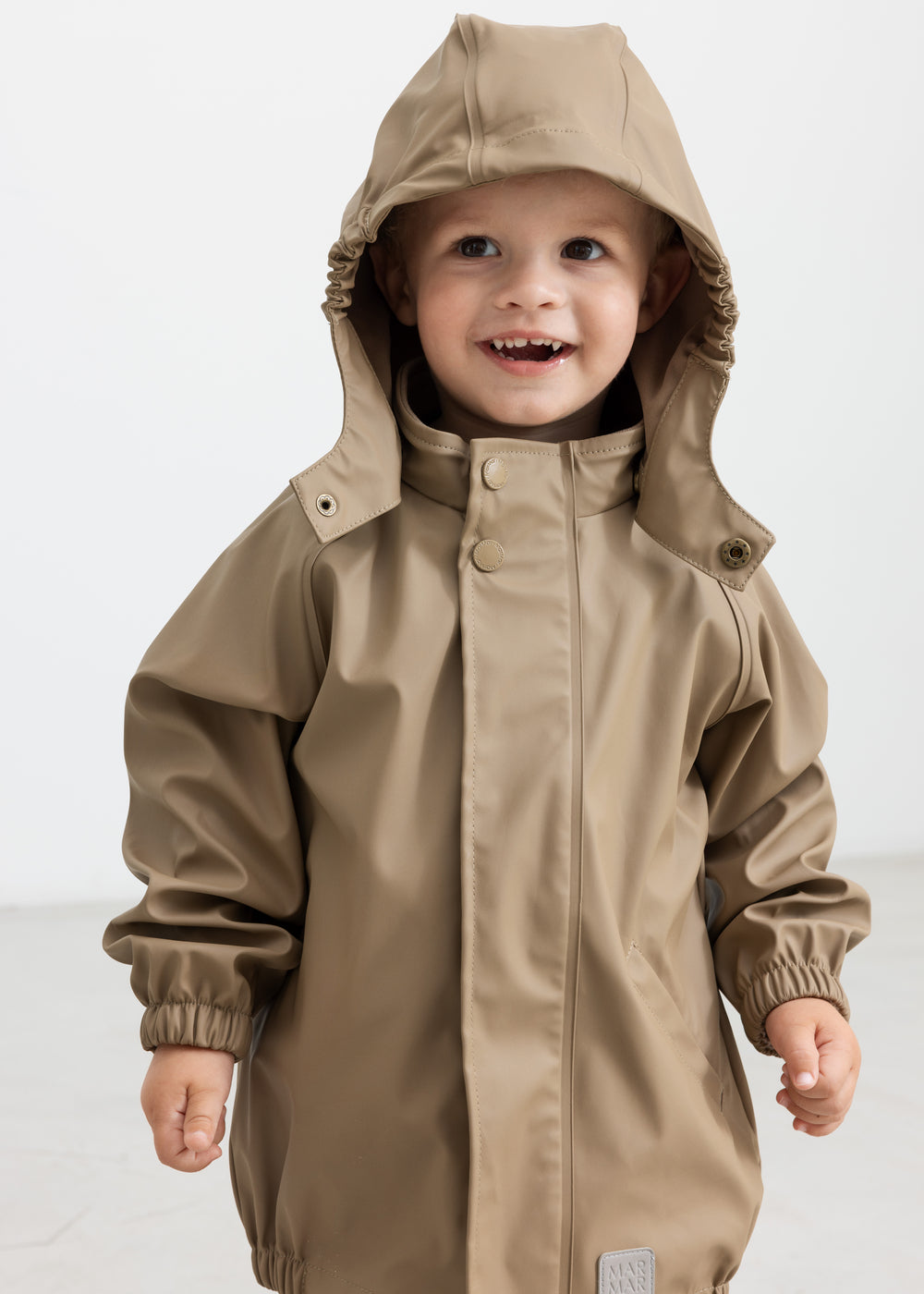 Barn iført beige regnsæt med hætte oppe, smilende
