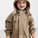 Barn iført beige regnsæt med hætte oppe, smilende