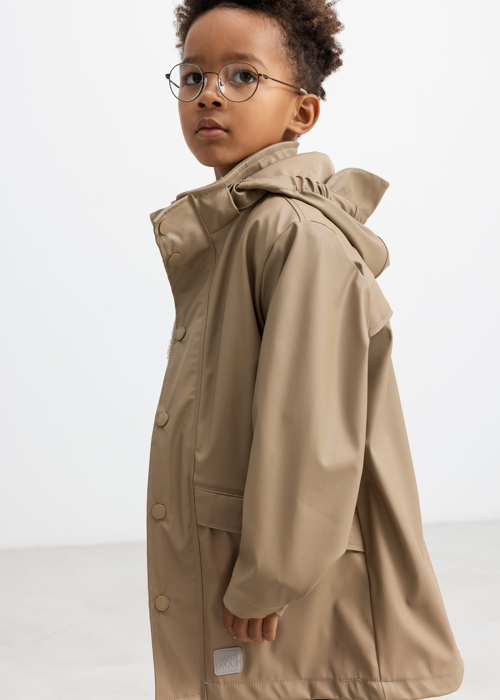 Barn iført beige regnjakke, set i profil med hætten oppe