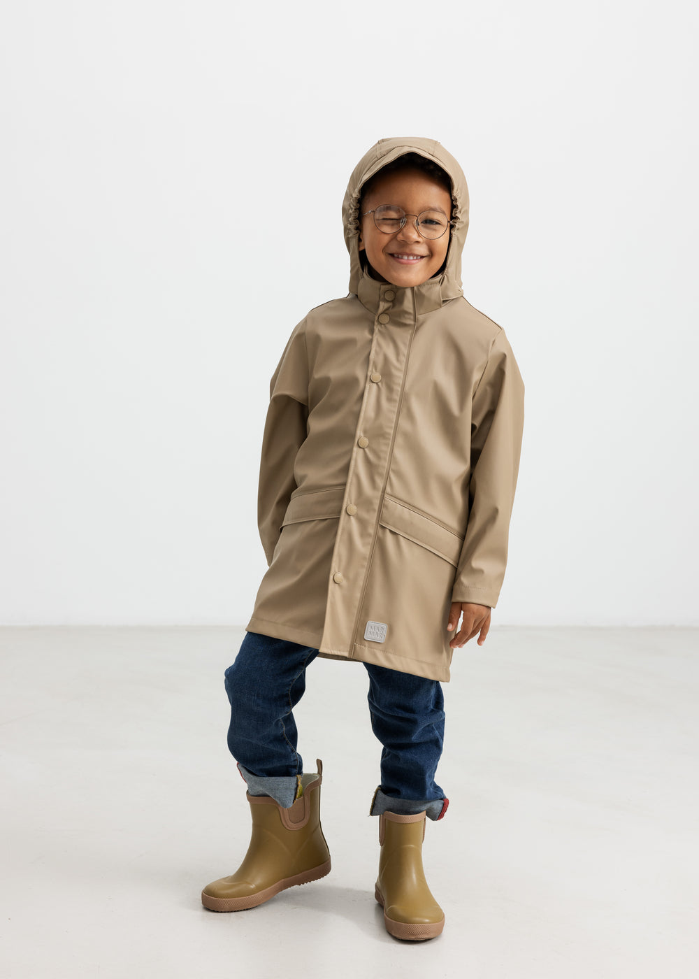 Barn iført beige regnjakke og gummistøvler, smilende
