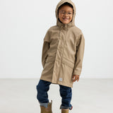 Barn iført beige regnjakke og gummistøvler, smilende