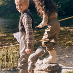 To børn går langs vandet iført beige regntøj