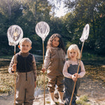 Tre børn med fiskenet iført beige regntøj i naturen