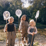 Tre børn med fiskenet iført beige regntøj i naturen