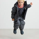 Børn hopper iført mørkegråt regnsæt med prikker og lyserød trøje