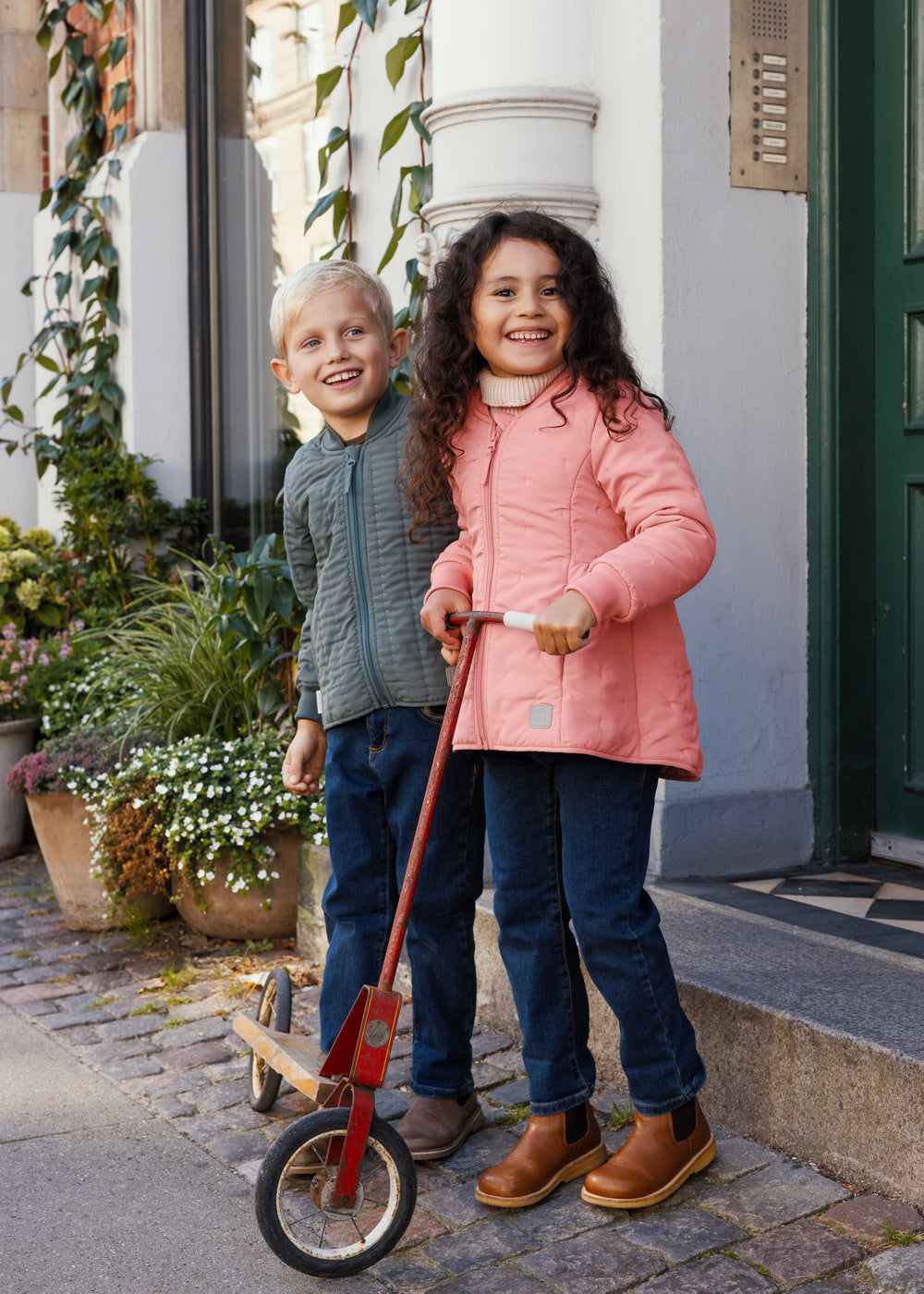To børn foran en dør, dreng iført støvet grøn termojakke, pige i lyserød