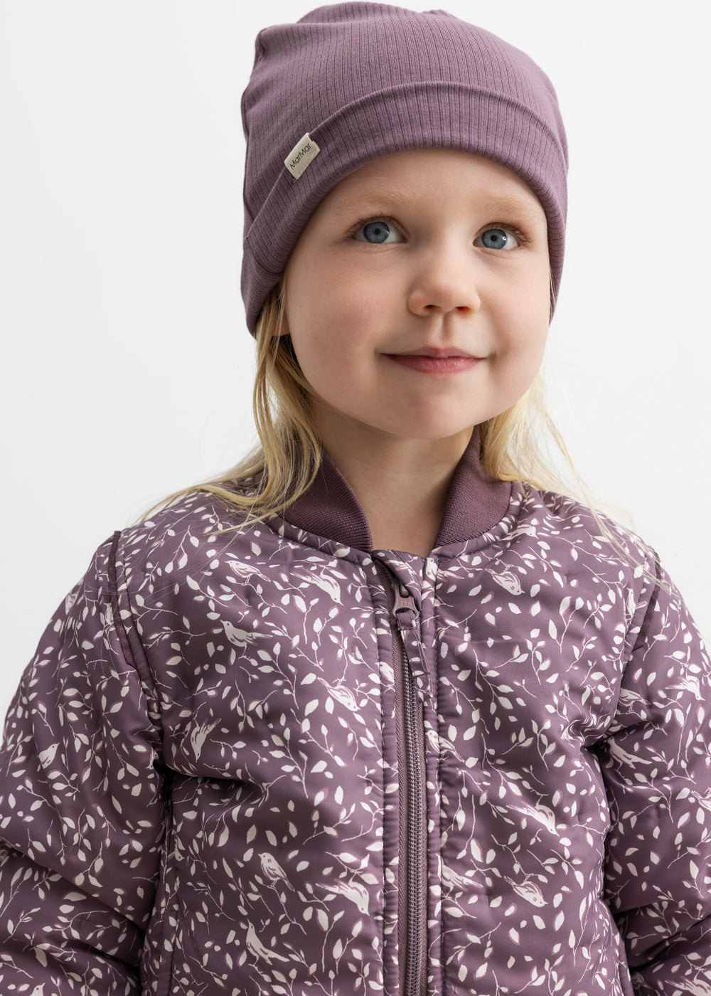 Barn iført lilla ribbeanie og jakke med print, smiler