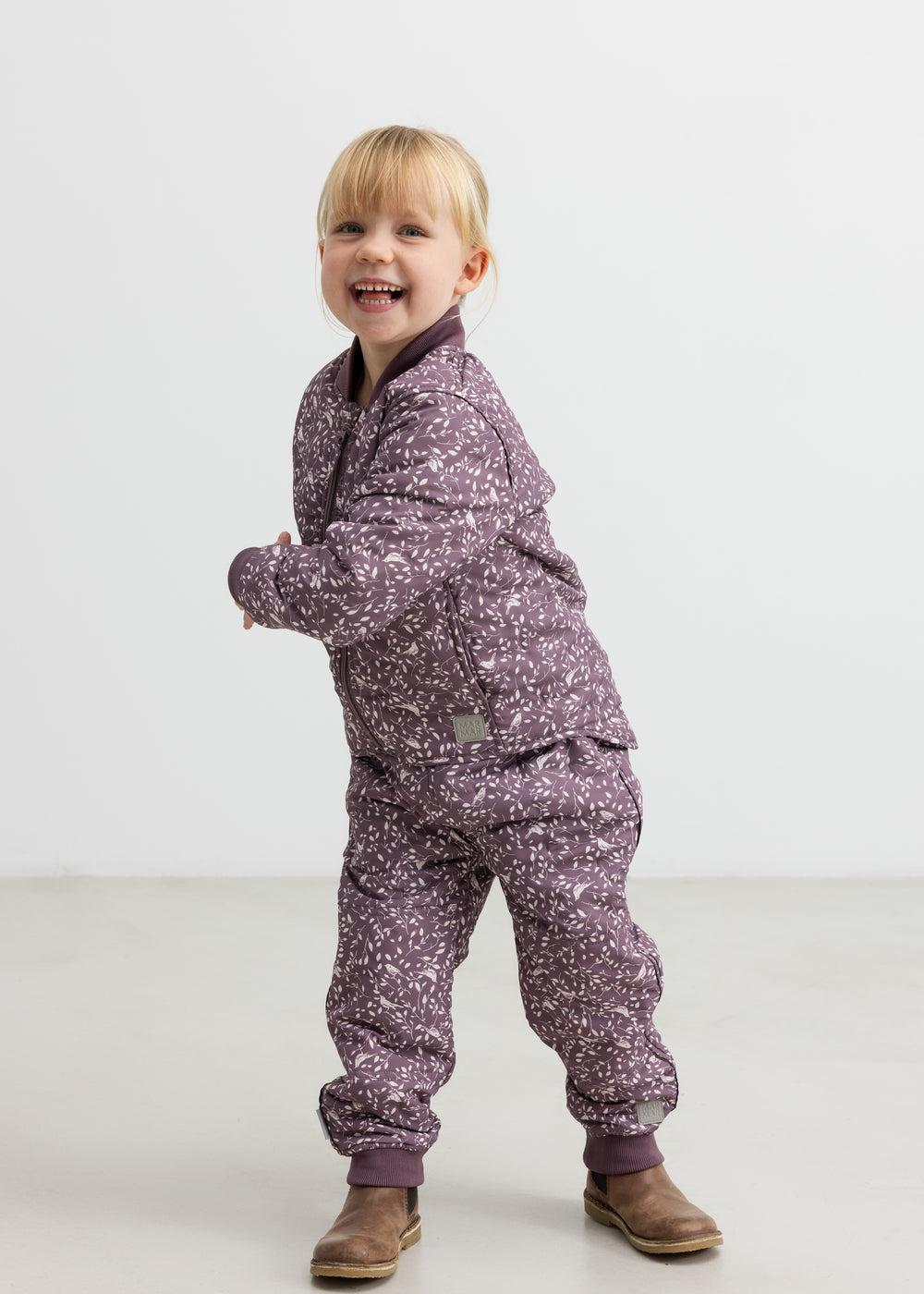 Barn iført matchende støvlilla termotøj, smilende og i bevægelse