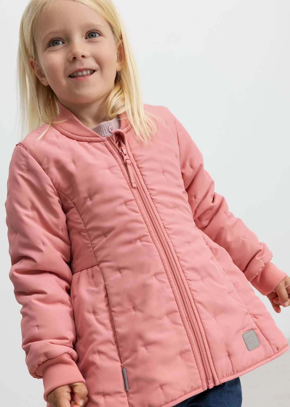 Barn iført lyserød termojakke, smilende og med hånden i lommen