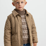 Barn iført brun termojakke og mønstret strik, kigger mod kameraet