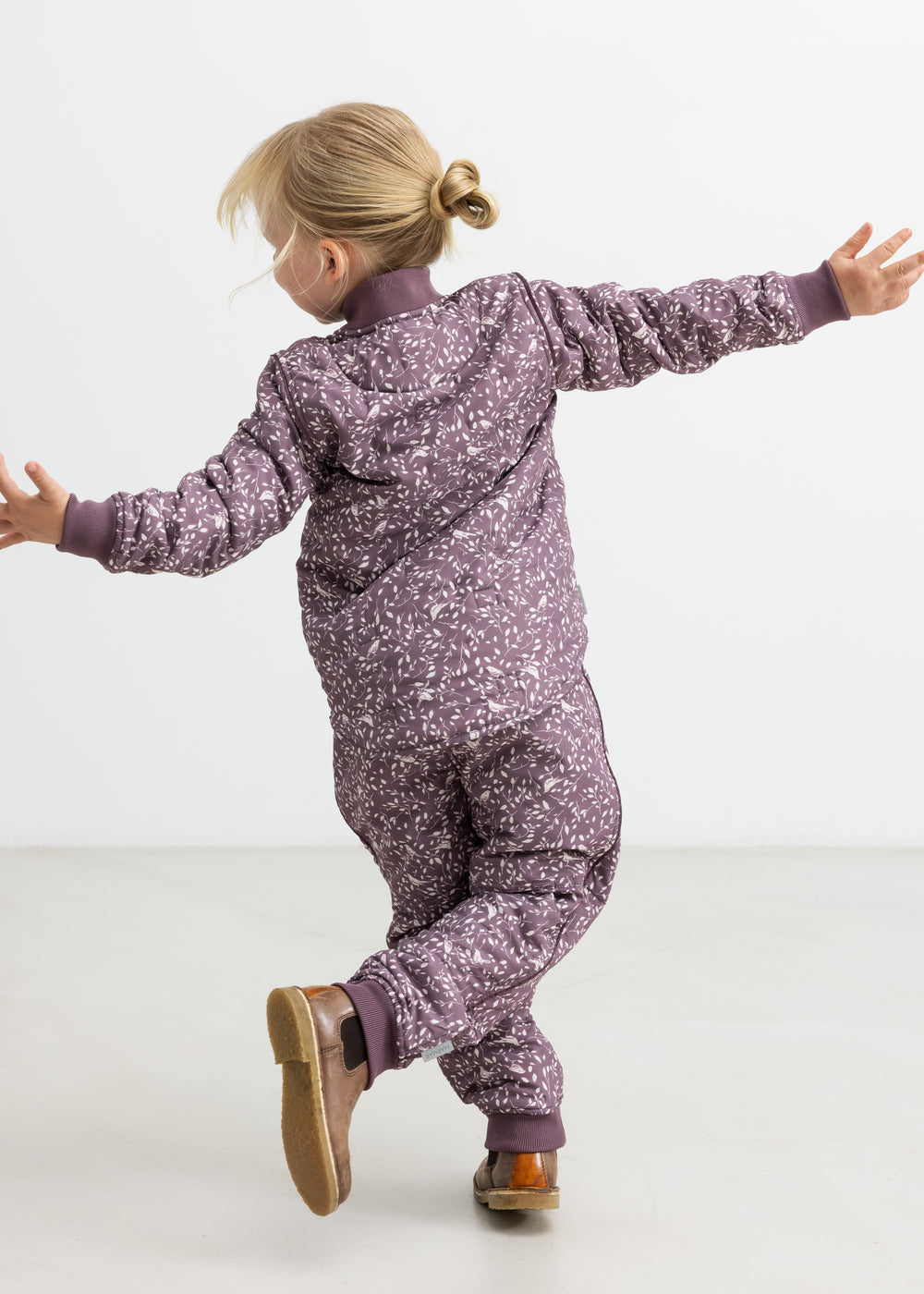Barn iført støvlilla termobukser og jakke med print, hopper med armene ud