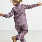 Barn iført støvlilla termojakke og bukser med print, hopper med armene ud