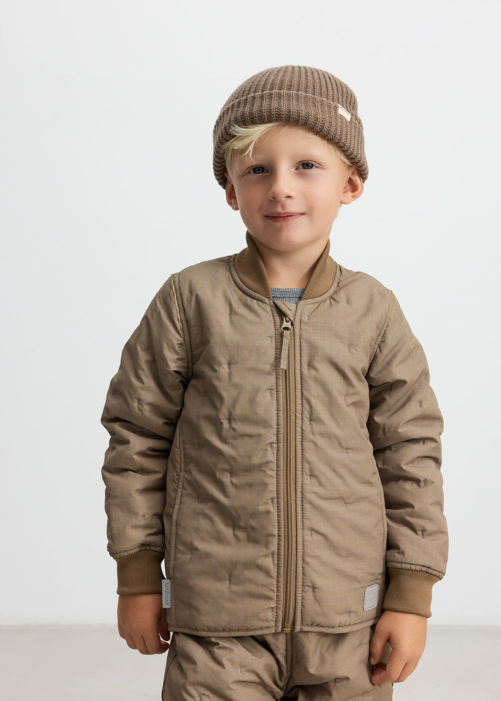 Barn iført brunternet termojakke og matchende bukser, smilende