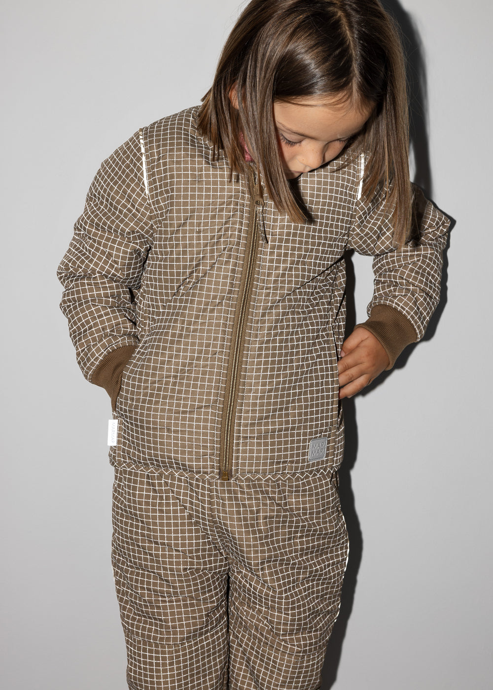 Pige iført brunternet termojakke, ser ned og har hænderne i lommerne