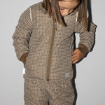 Pige iført brunternet termojakke, ser ned og har hænderne i lommerne