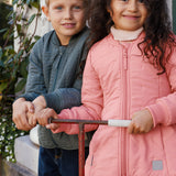 o børn holder en scooter, drengen iført støvet grøn termojakke og pigen lyserød