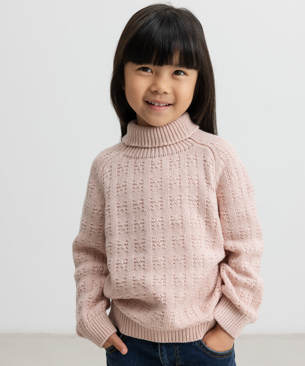 Barn iført lyserød striktrøje med rullekrave og mørkeblå jeans, smilende