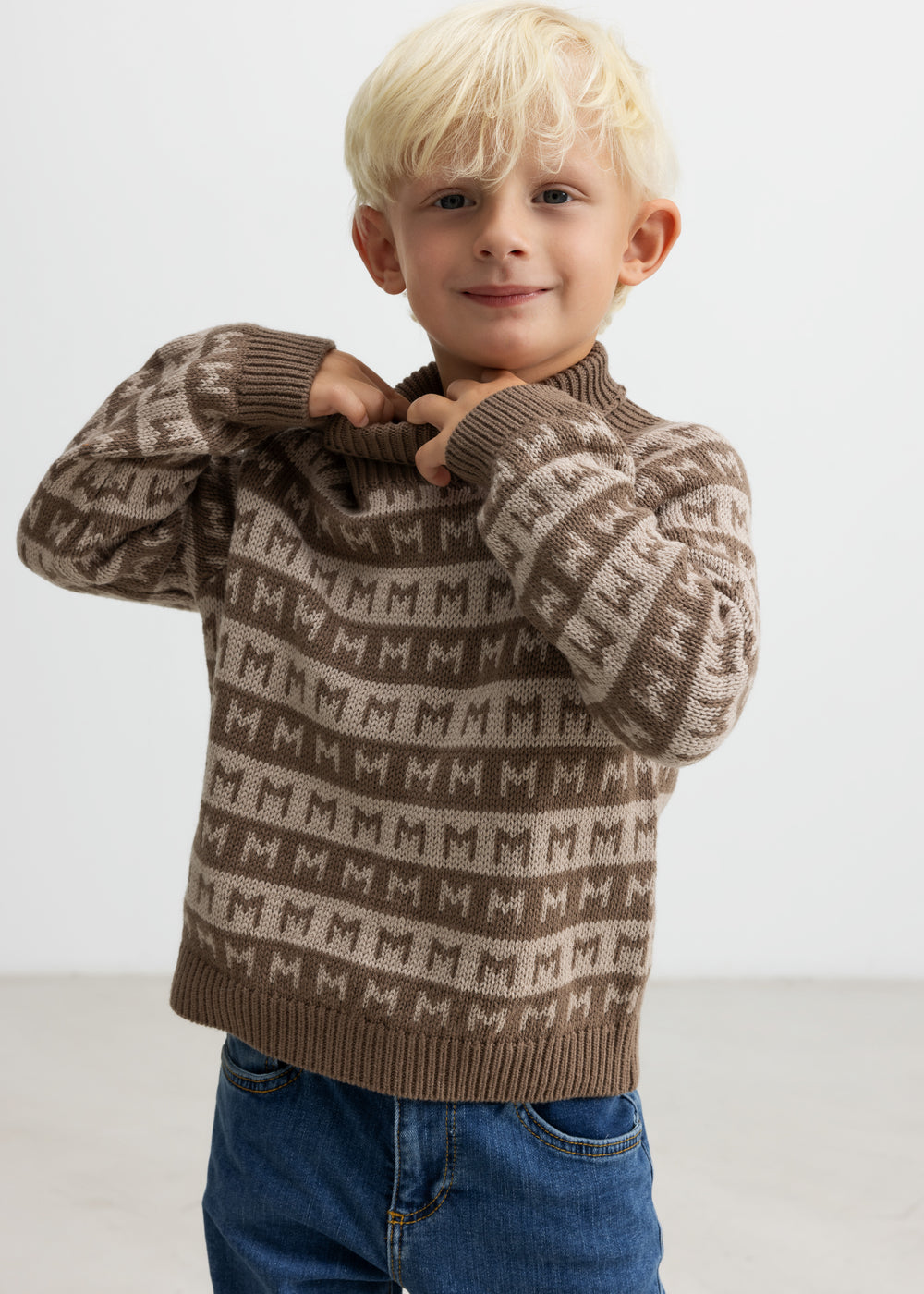 Barn tager en brun M-mønstret striktrøje på, smilende