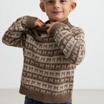 Barn tager en brun M-mønstret striktrøje på, smilende