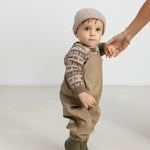 Barn iført beige strikhue og termotøj, håller en voksen i hånden