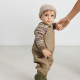 Barn iført beige strikhue og termotøj, håller en voksen i hånden