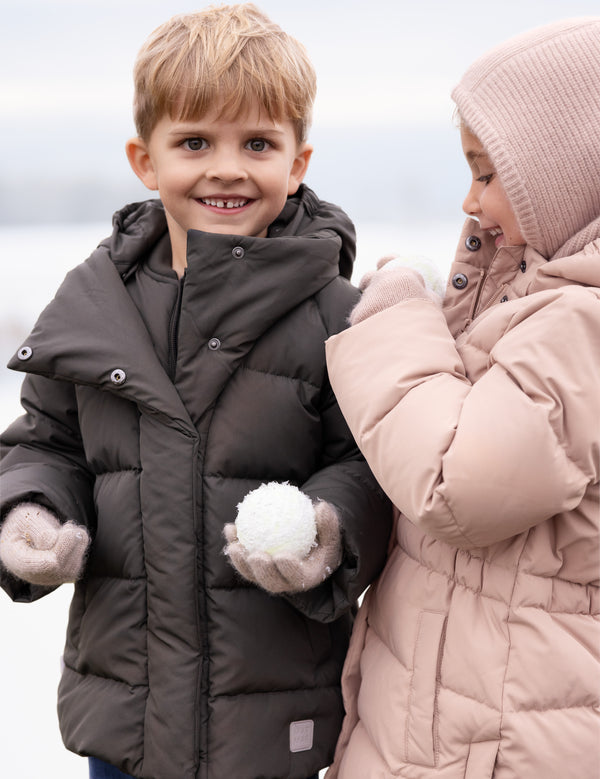 To børn iført pufferjakker leger i sneen med en snebold