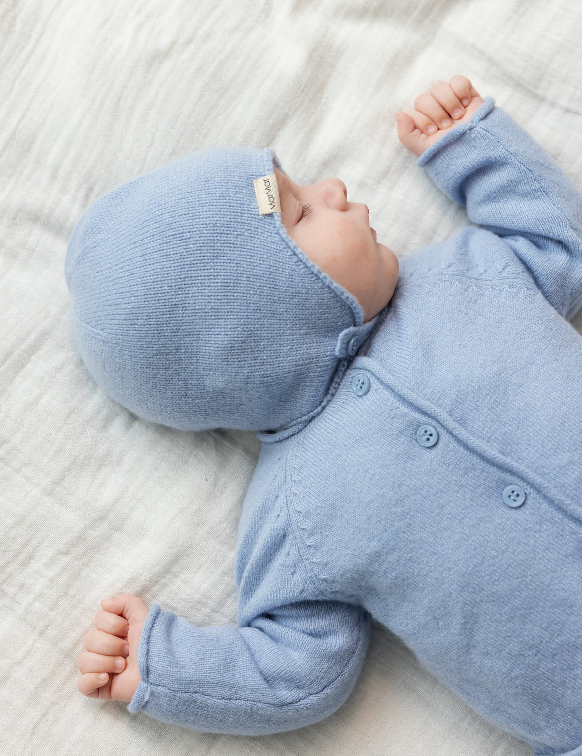 Nyfødt baby i lyseblå strikket cardigan og hue liggende på babytæppe