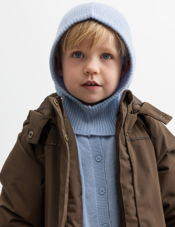 Barn iført brun jakke og lyseblå elefanthue